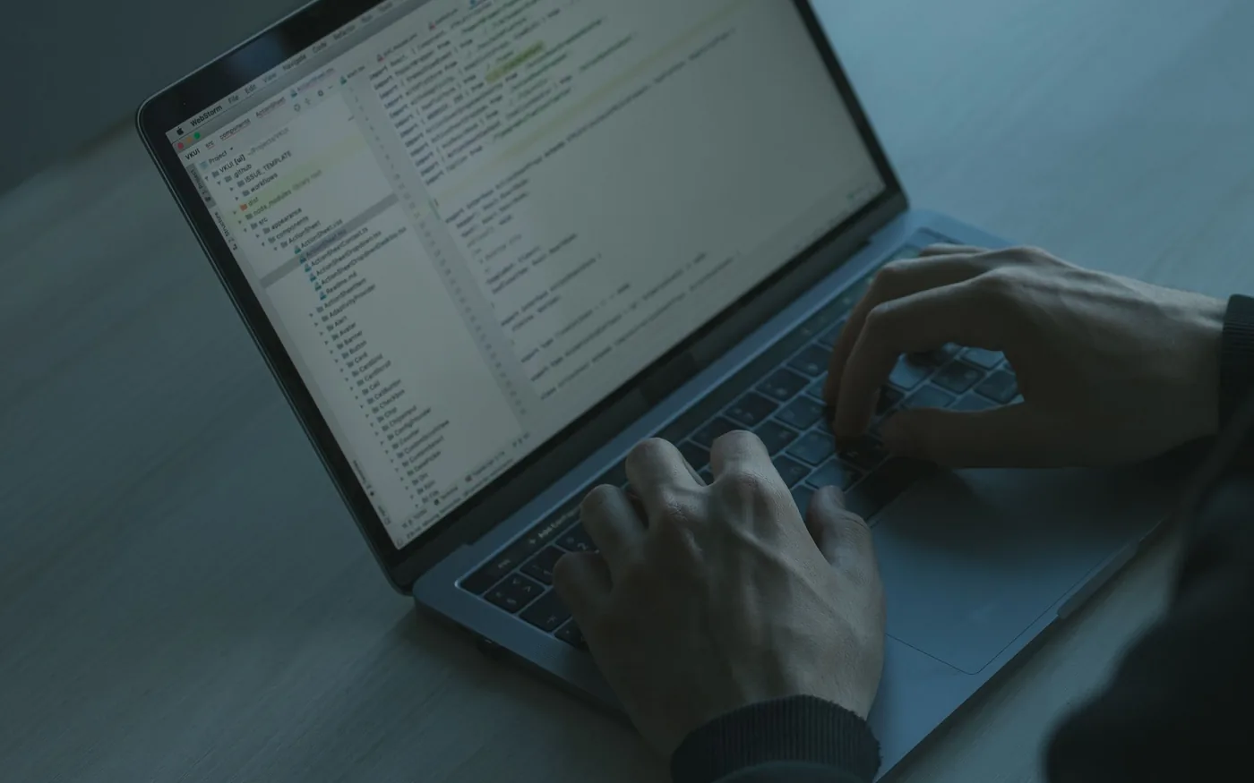 Hands typing on a laptop in a dimly lit technology workspace
